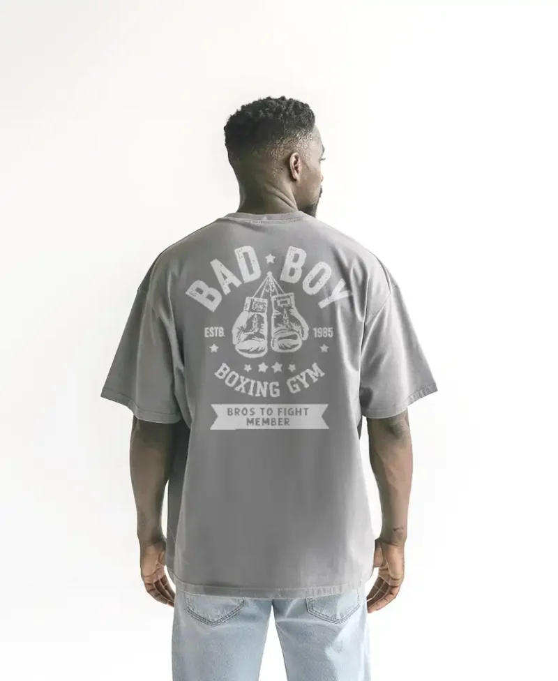 chico modelo en camiseta gris claro oversize con diseno de color blanco, bad boy, edicion limitada, vista trasera