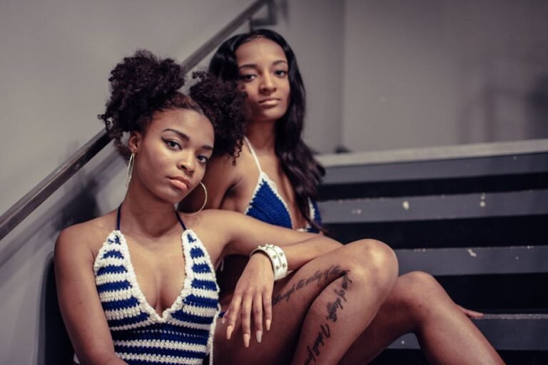 Chic and stylish portrait of two women wearing trendy crochet tops, seated on a staircase.