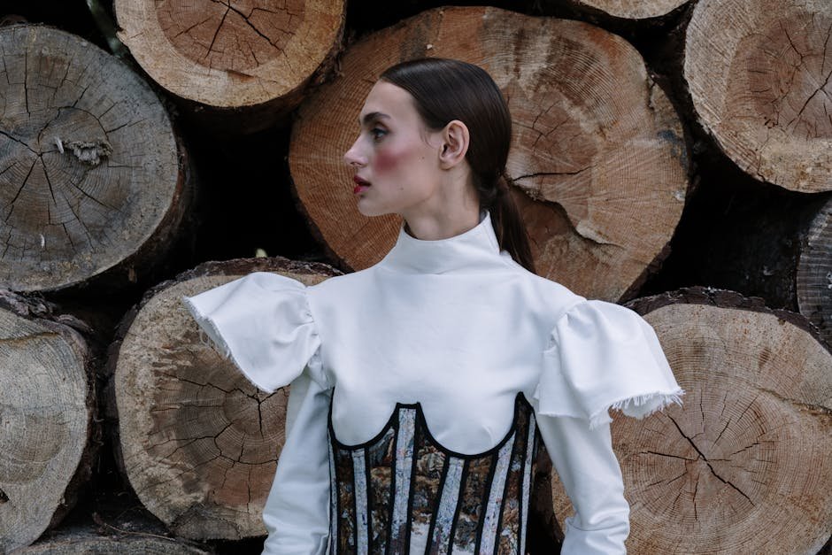 A stylish woman in an elegant dress poses against a backdrop of stacked logs.