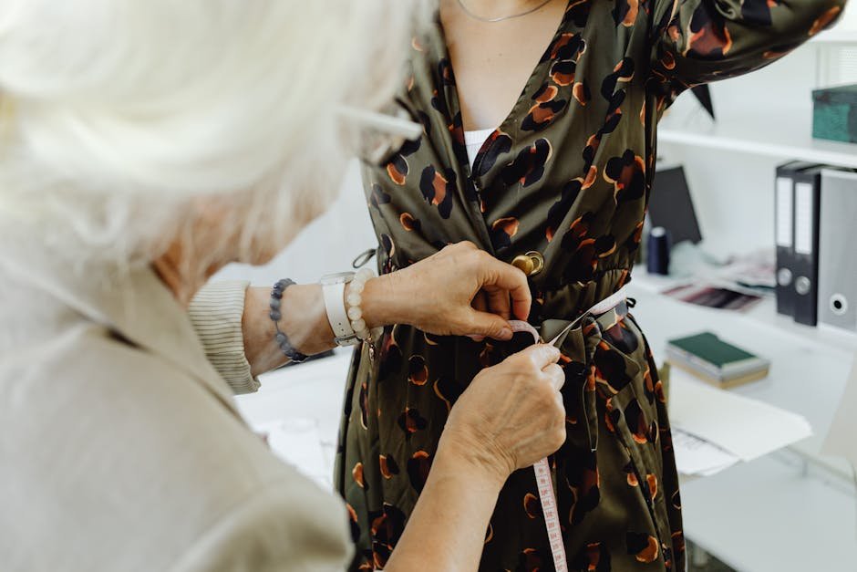An elderly seamstress measures a woman's waist for a custom dress fitting.